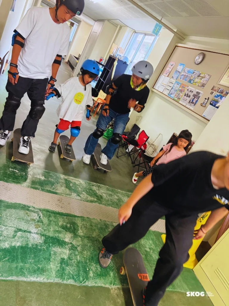 ヘルメットとプロテクターを着けて、親子でスケートボードの上に立つ練習